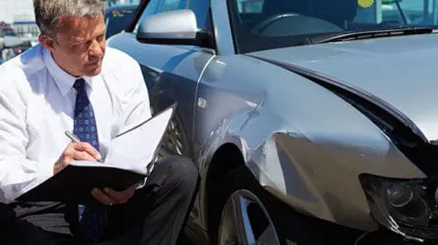 Man-Reading-Insurance-Forms-While-Looking-at-Damaged-Car